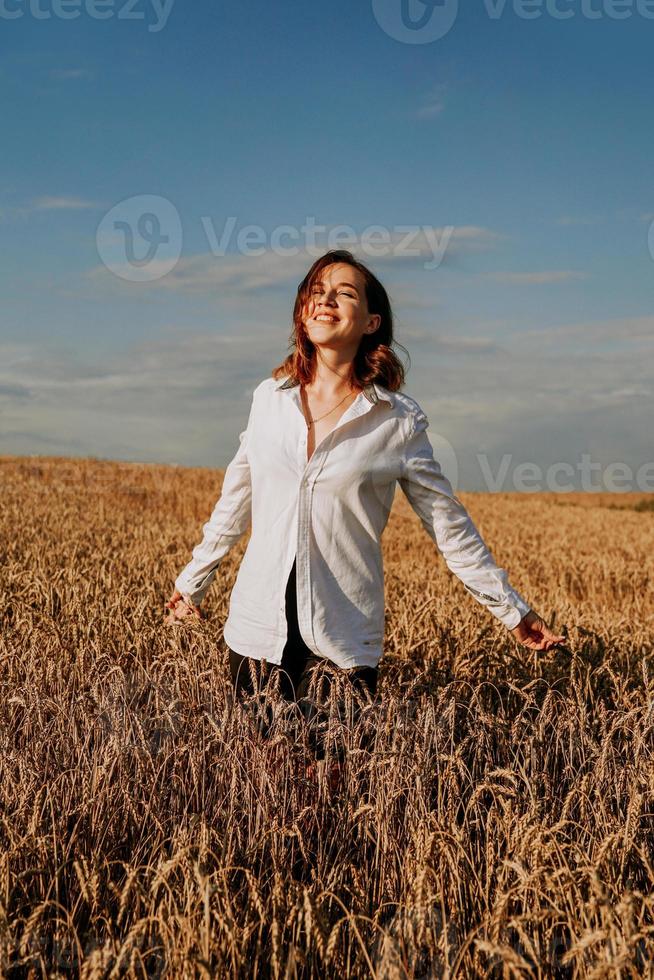 Happy young woman in a white shirt in a wheat field. Sunny day. photo