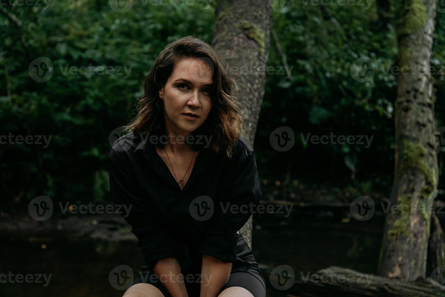 Young woman - close portrait in a dark forest. Woman in black shirt photo