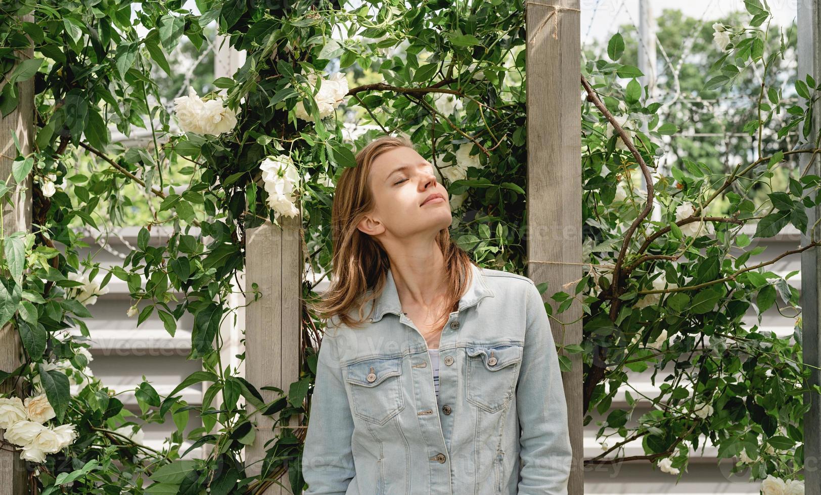Young woman standing in white roses in a garden or park photo