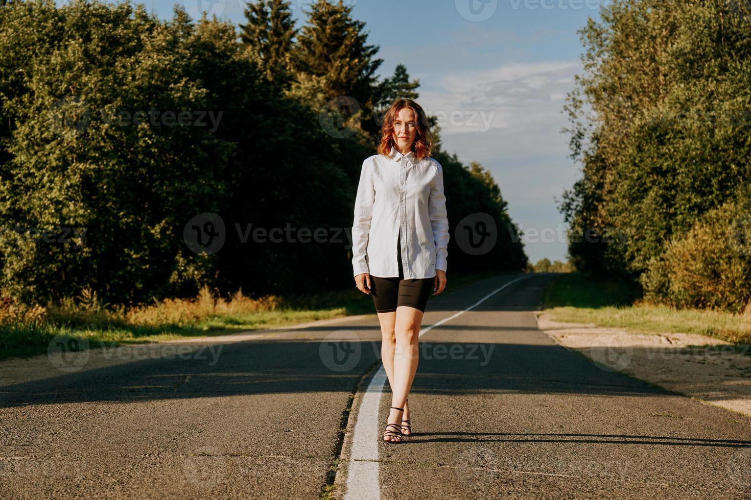 mujer con una camisa blanca camina por la carretera entre el bosque foto