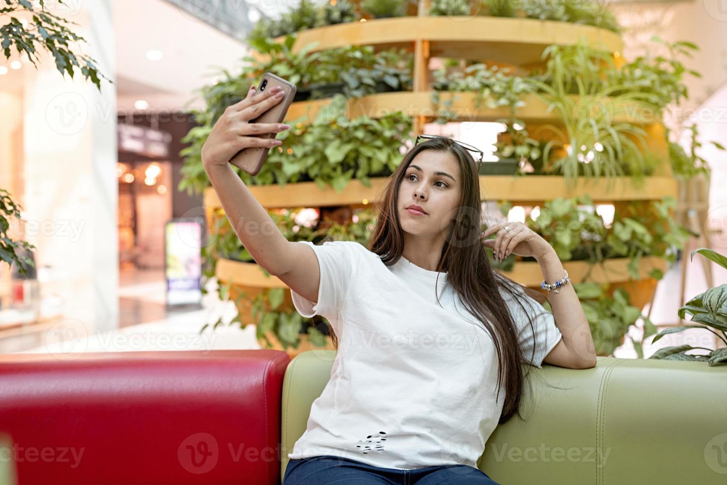 mujer sentada en el sofá en el centro comercial, mirando el teléfono foto