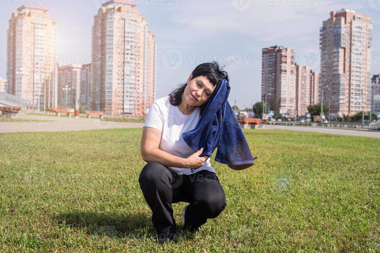 Senior woman wiping out sweat after hard workout outdoors in the park photo