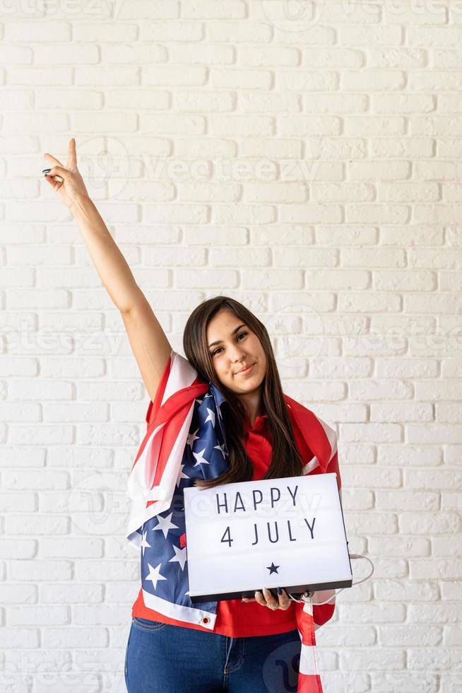 Mujer con bandera americana sosteniendo lightbox con palabras feliz 4 de julio foto