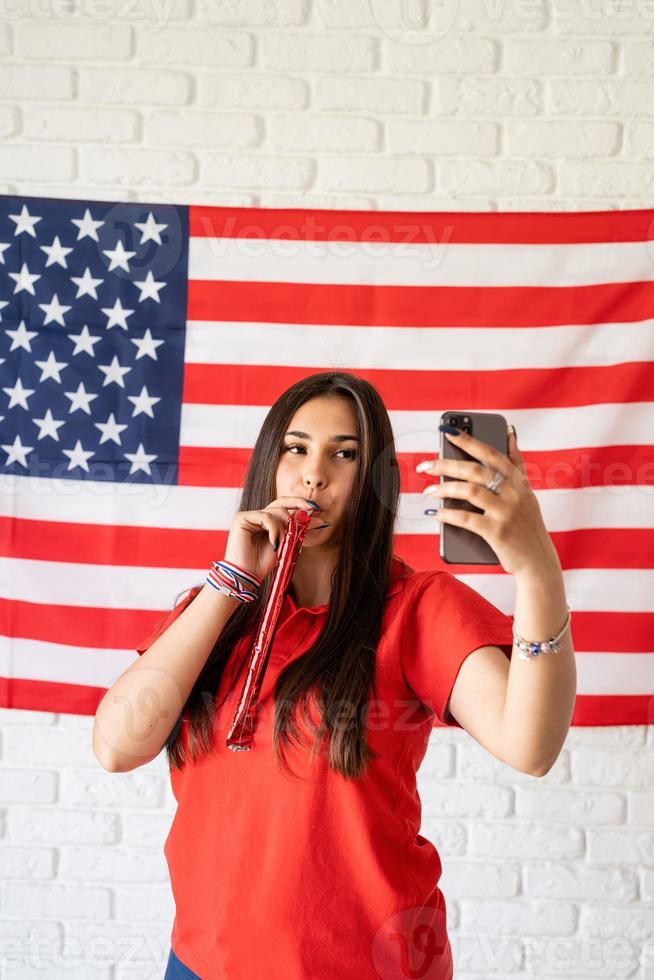 Mujer con un matraca tomando un selfie en el fondo de la bandera de Estados Unidos foto