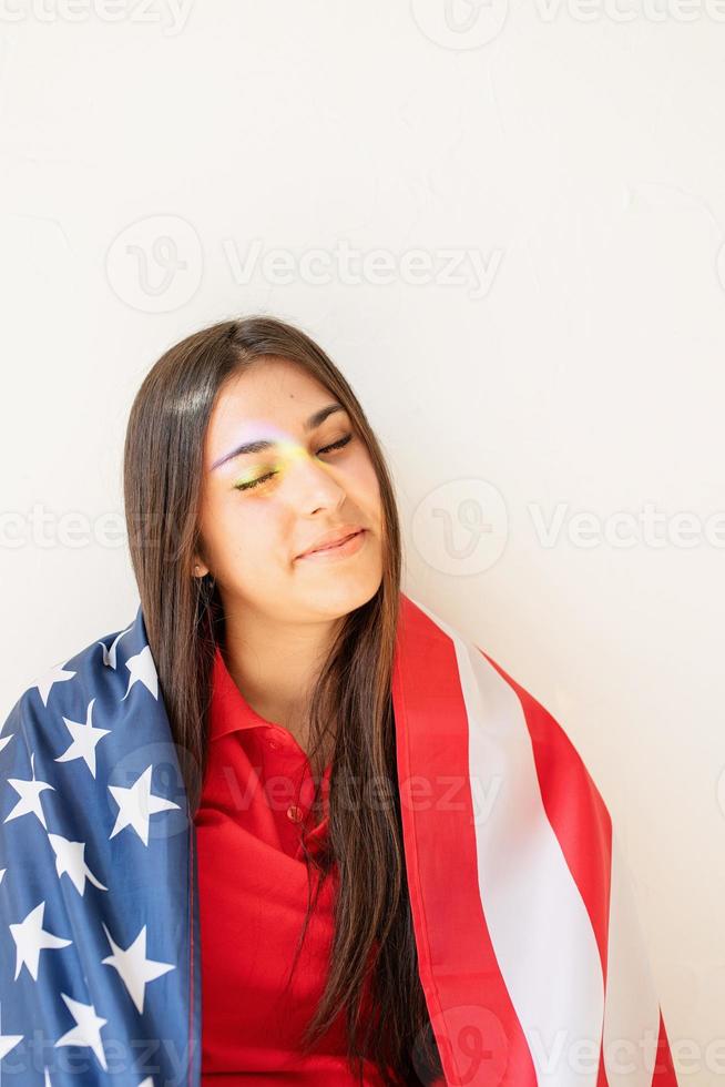 hermosa mujer joven con la bandera americana y la reflexión del arco iris foto