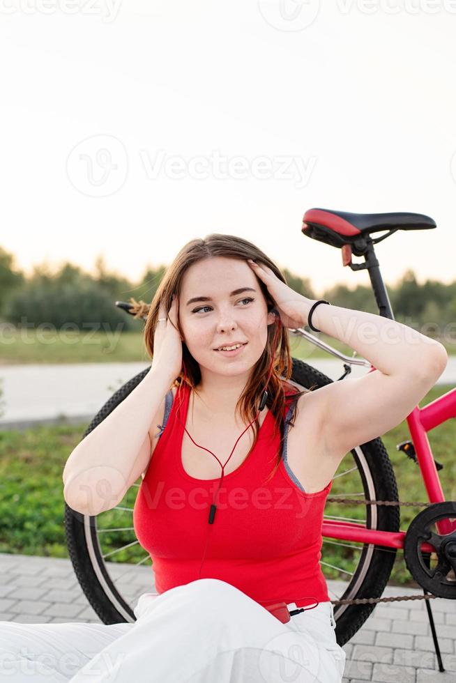 niña sentada junto a su bicicleta escuchando música en el parque foto