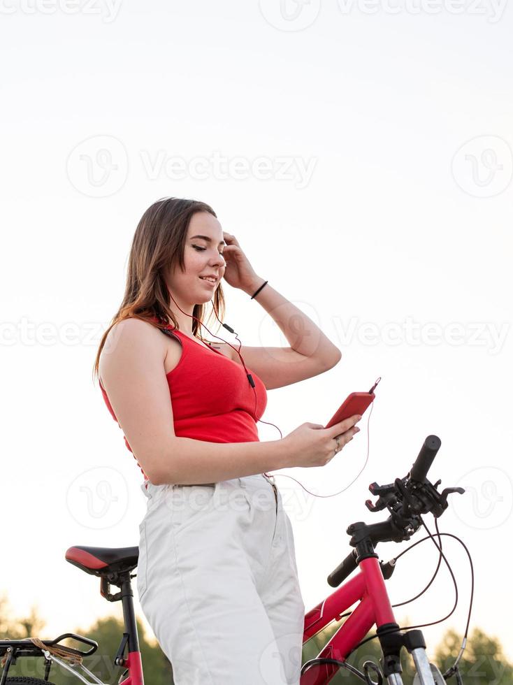 Girl standing next to her bike listening to the music in headphones photo