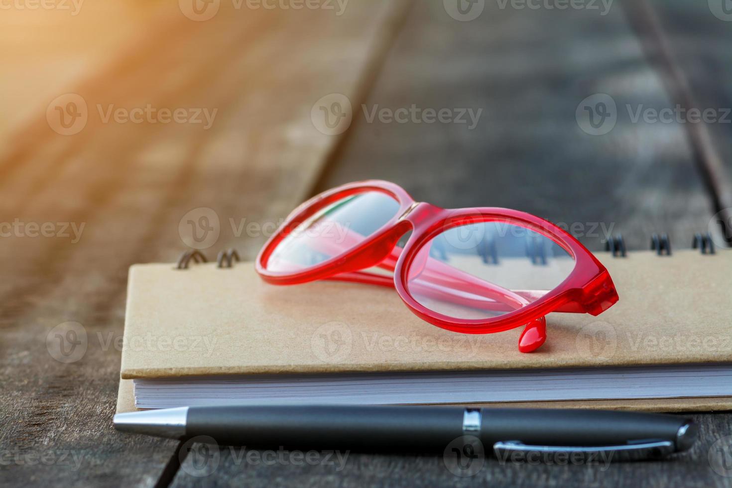 Gafas rojas en el cuaderno con bolígrafo y fondo de madera foto