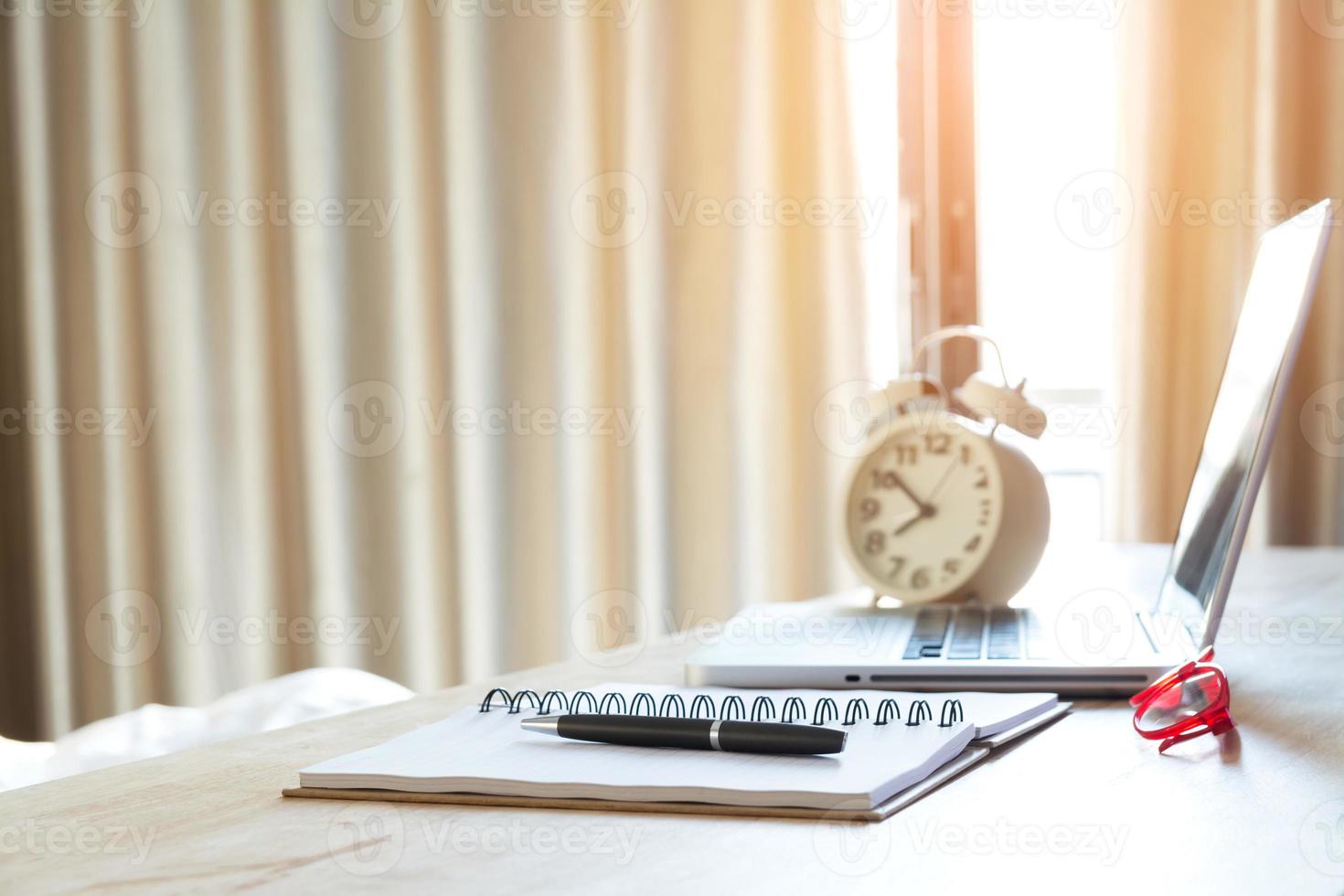 Pen, Notebook, Glasses and Laptop with Alarm Clock on Desk photo