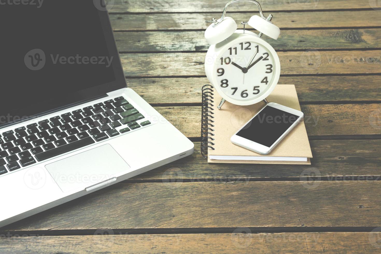 Laptop, notebook, smartphone and alarm clock on wooden table photo