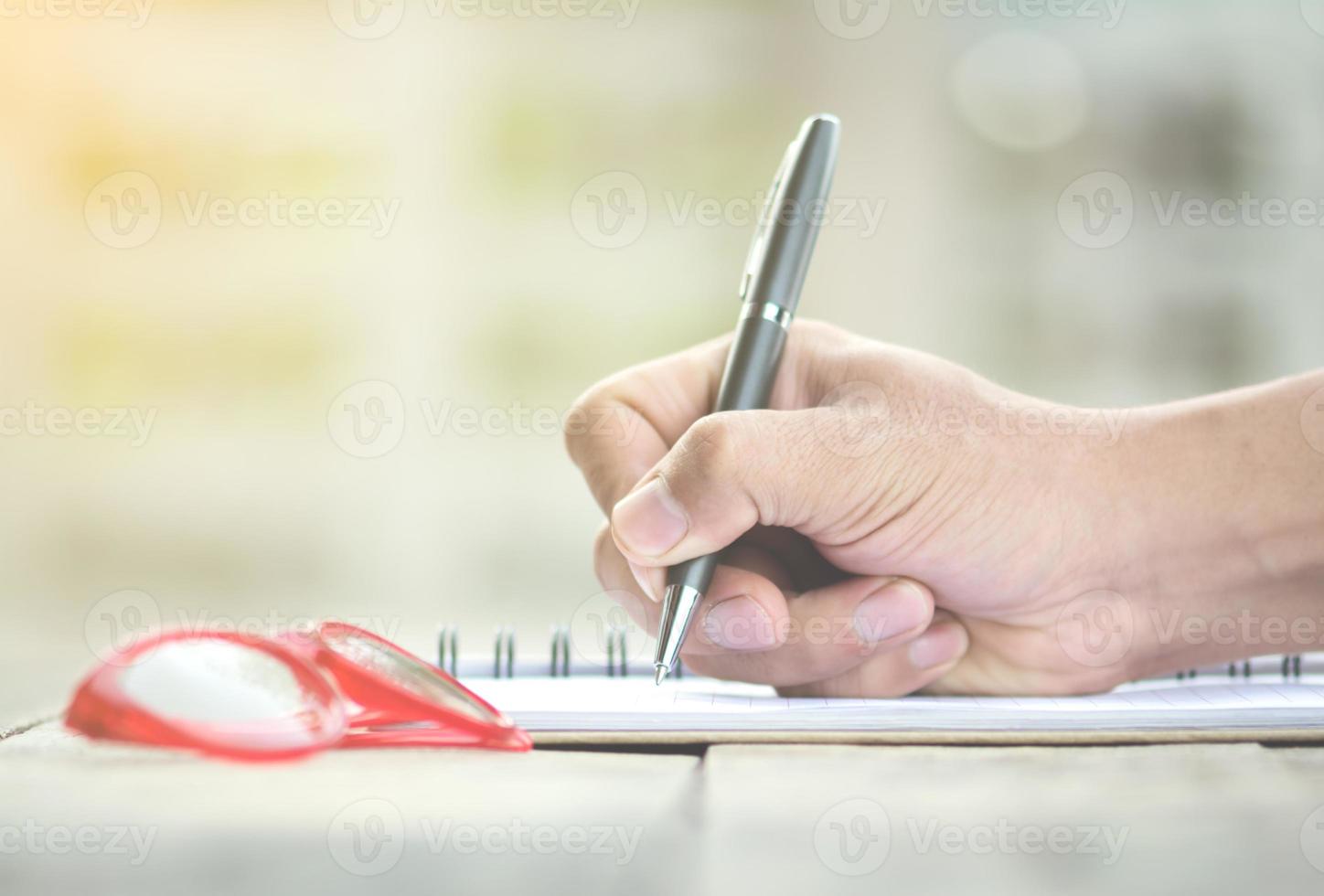 Persona escribiendo notas con gafas en el escritorio foto