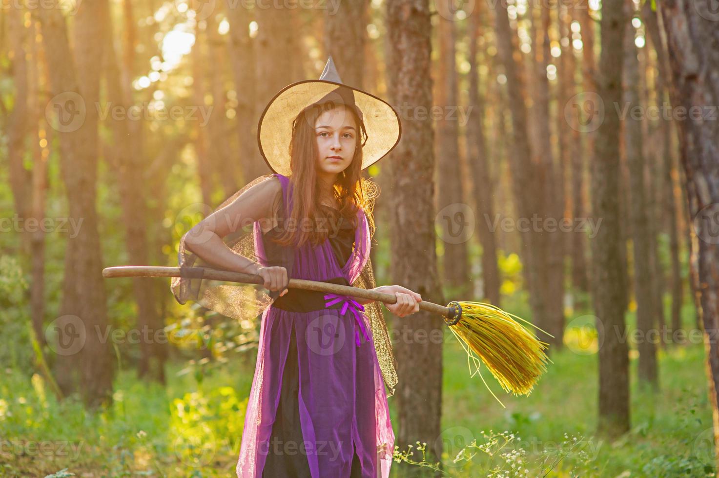 niña en un disfraz de halloween en el bosque con una escoba. foto