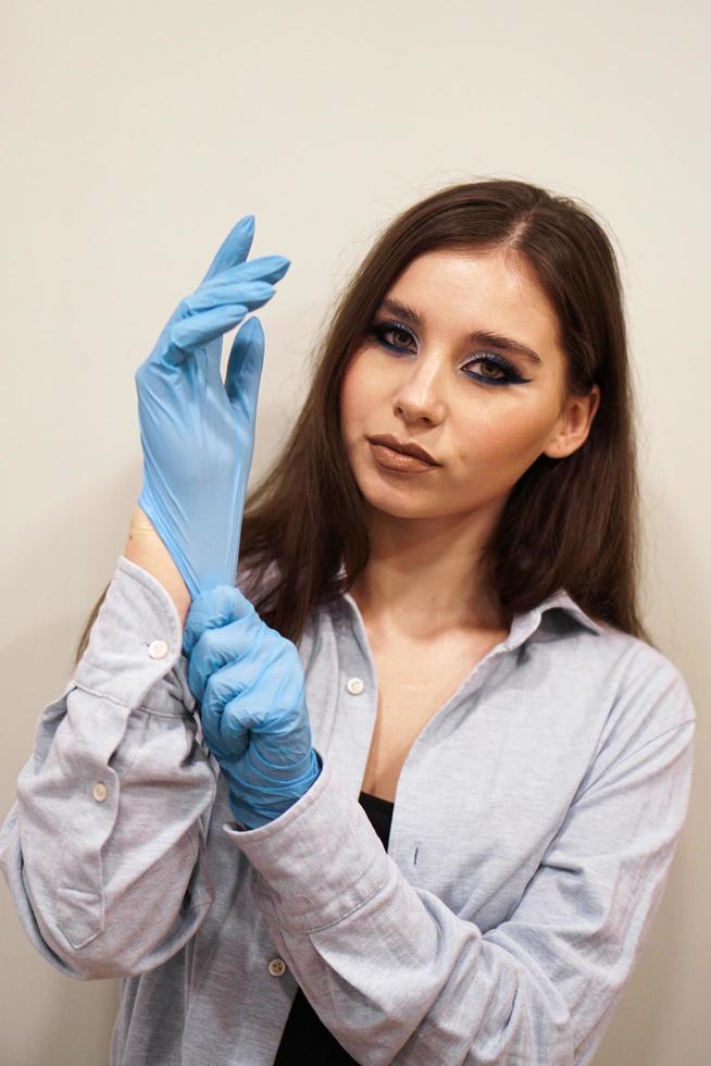 Mujer atractiva con maquillaje elegante poniéndose las manos guantes de látex foto