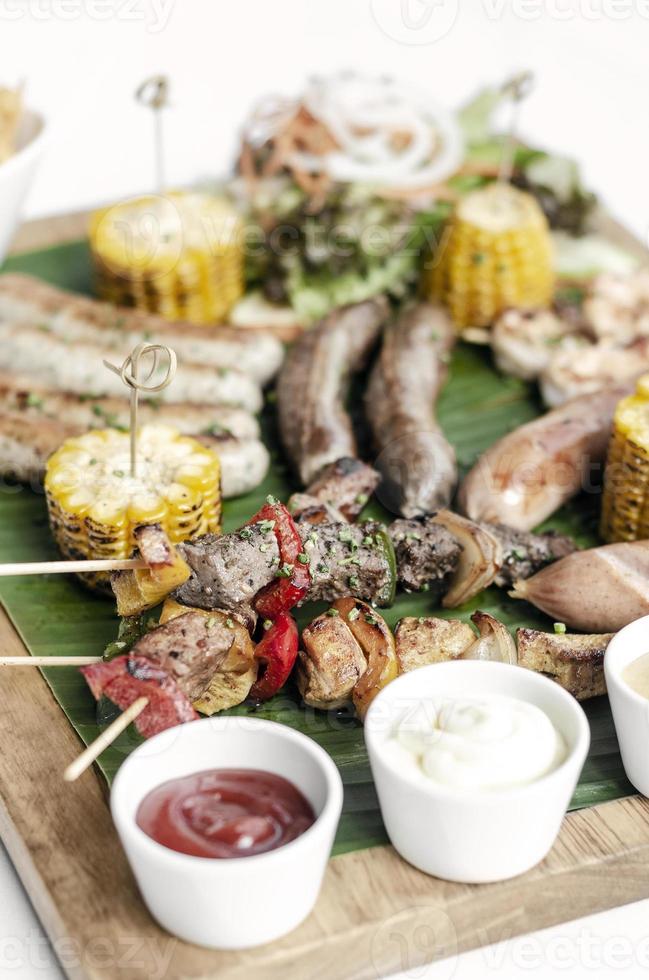 Parrillada orgánica parrillada plato de carne comida rústica con salchichas, brochetas, guarniciones y salsas foto