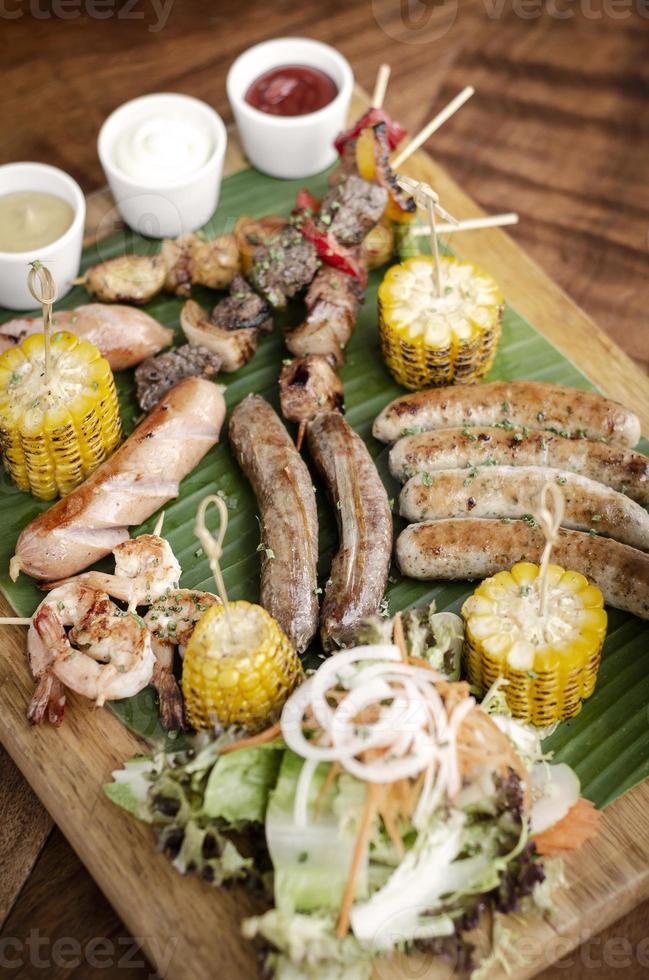 Parrillada orgánica parrillada plato de carne comida rústica con salchichas, brochetas, guarniciones y salsas foto