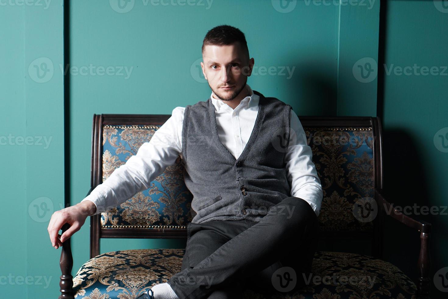 Handsome fashionable man in a white shirt sits on a chair in a studio photo