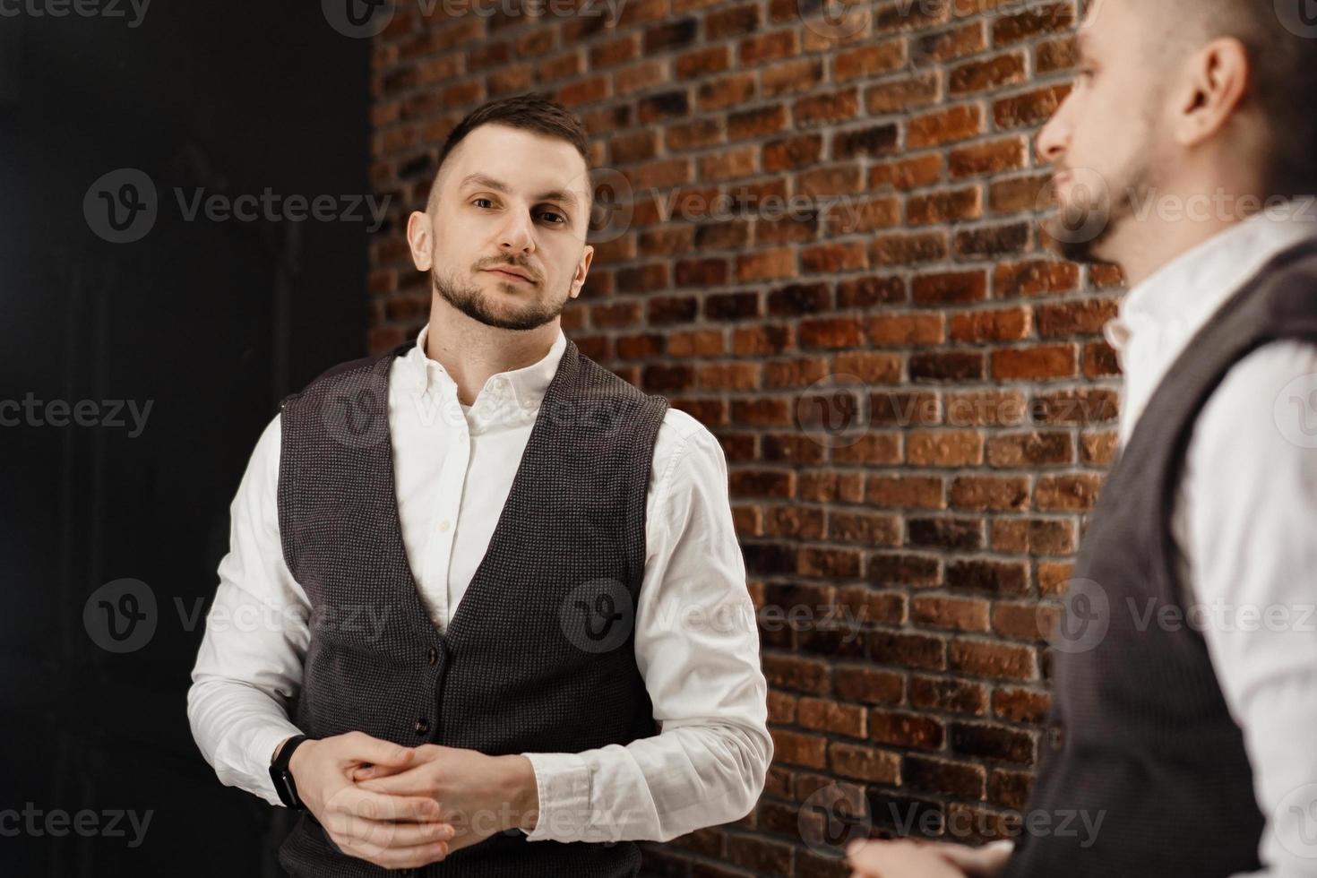 Stylish confident young man looking at himself in mirror photo