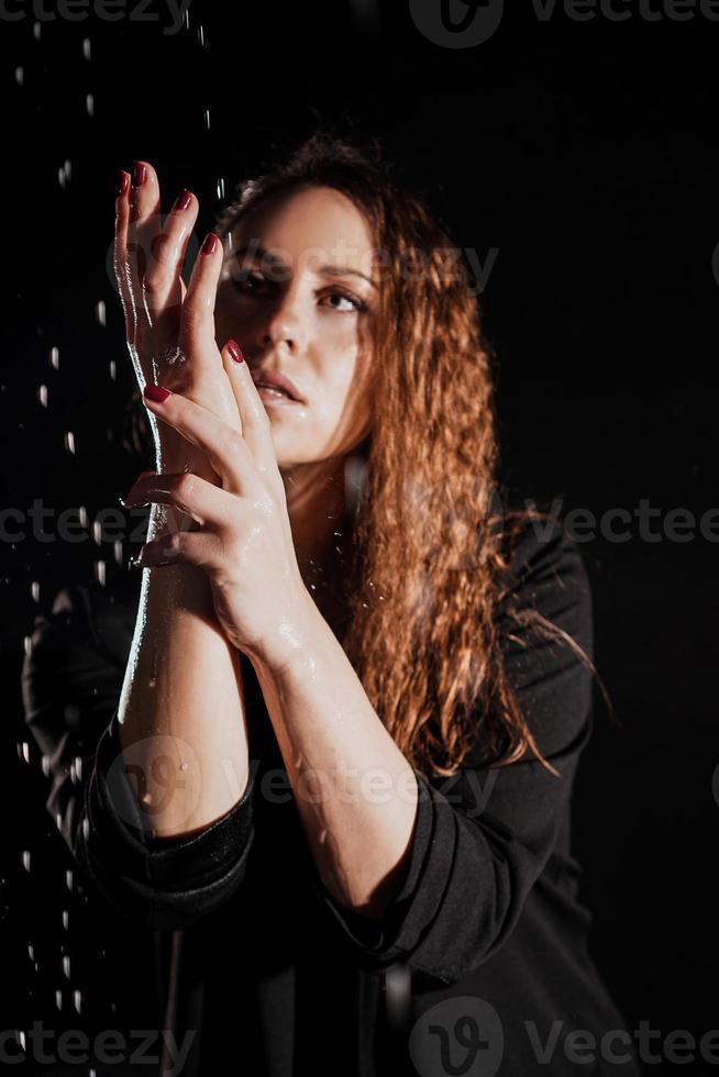 Wet beautiful woman in a black jacket under the falling drops of rain photo