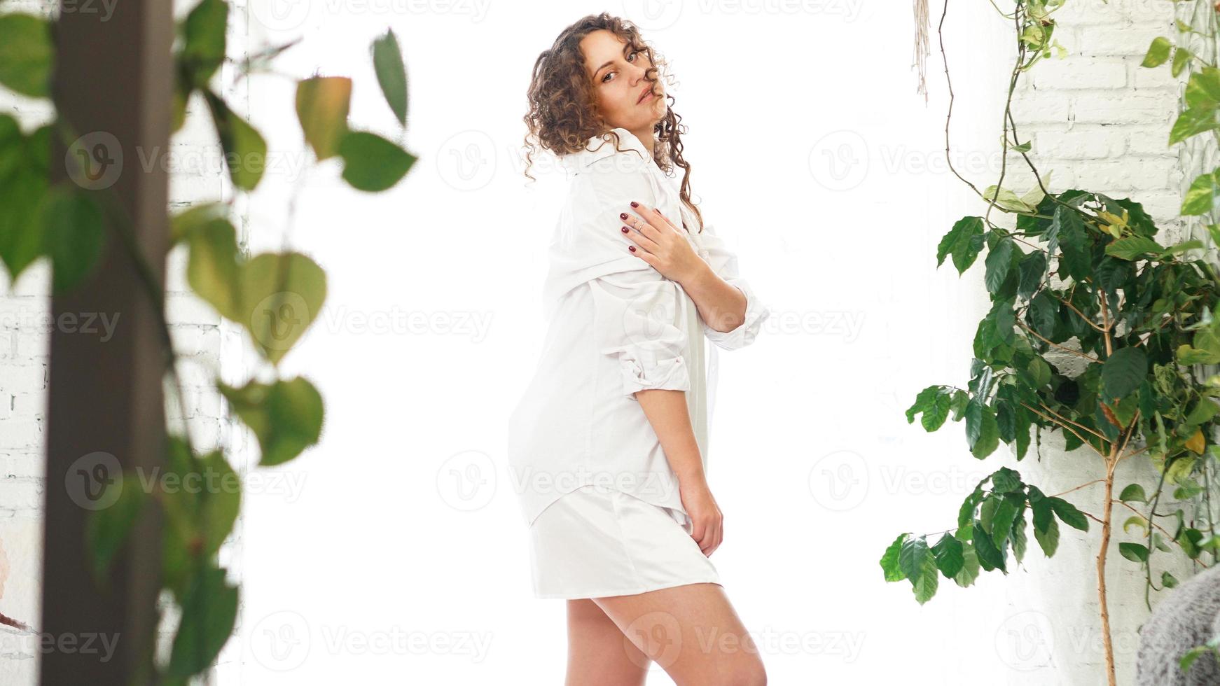 sexy, mujer joven, en, camisa blanca, en, dormitorio, con, plantas verdes foto