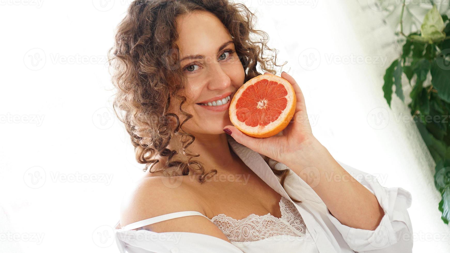 Portrait of pretty middle-aged woman with curly hair with grapefruit photo