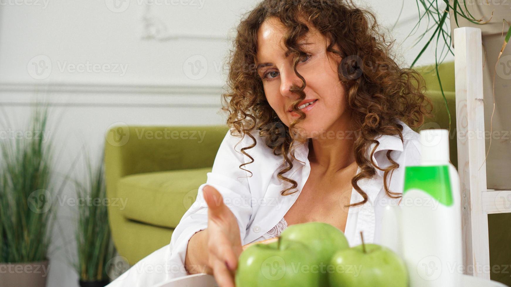 mujer con pelo rizado en habitación con sofá verde. manzanas y cuidado orgánico foto