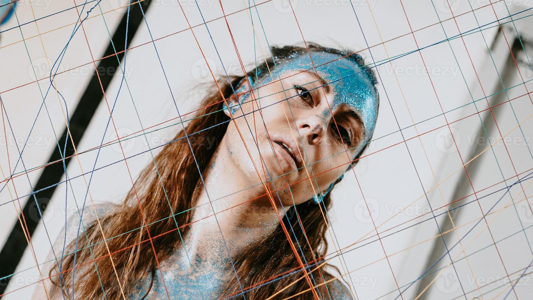 Brunette girl behind the threads net. Woman with blue sparkles photo