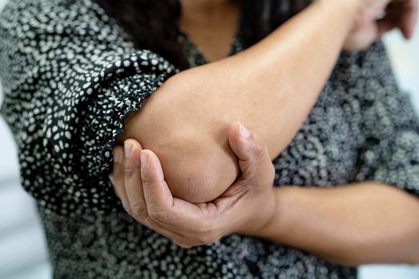 Paciente mujer asiática tocar y sentir dolor en el codo y el brazo foto
