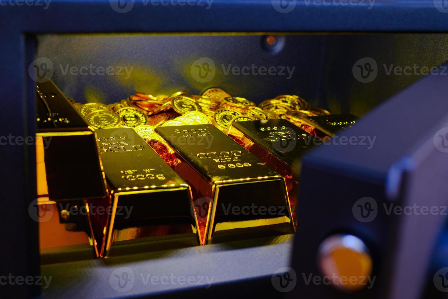 Caja fuerte de acero llena de pila de monedas y barra de oro sobre la mesa de madera foto