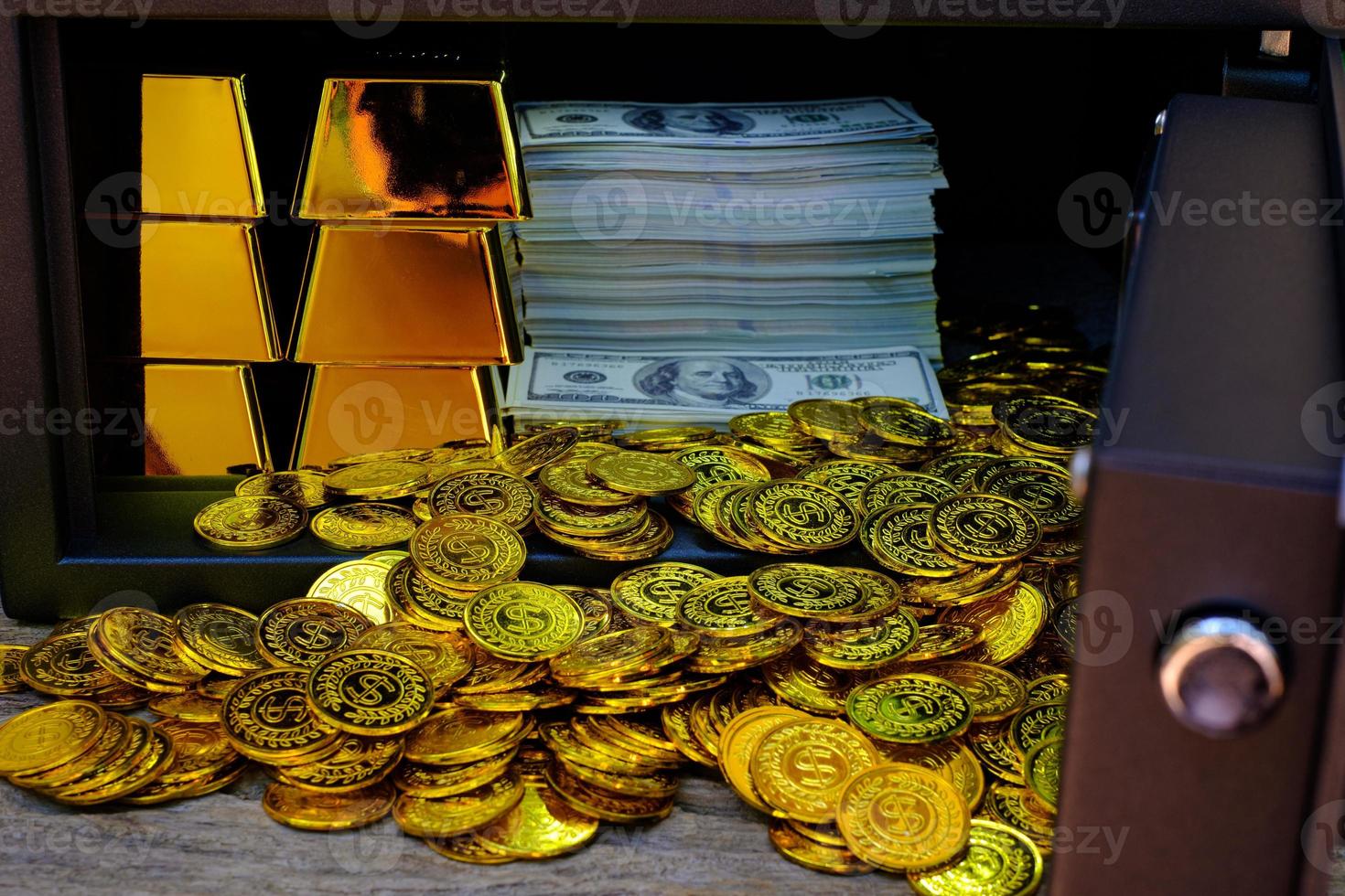Caja fuerte de acero llena de pila de monedas y barra de oro y billete de 100 usd foto