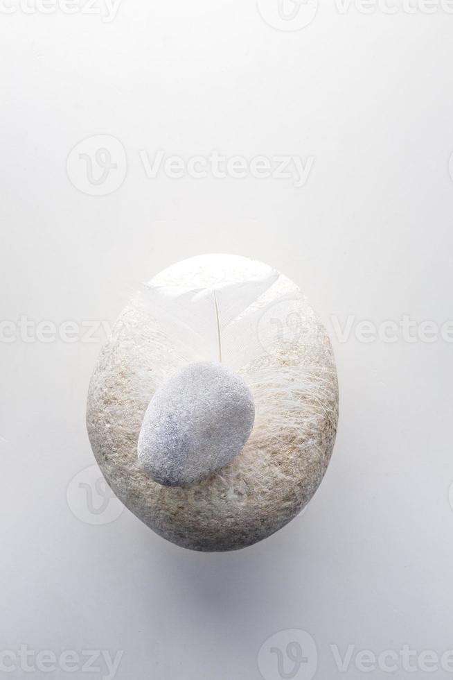 Top view of white stone and feather on a white background photo