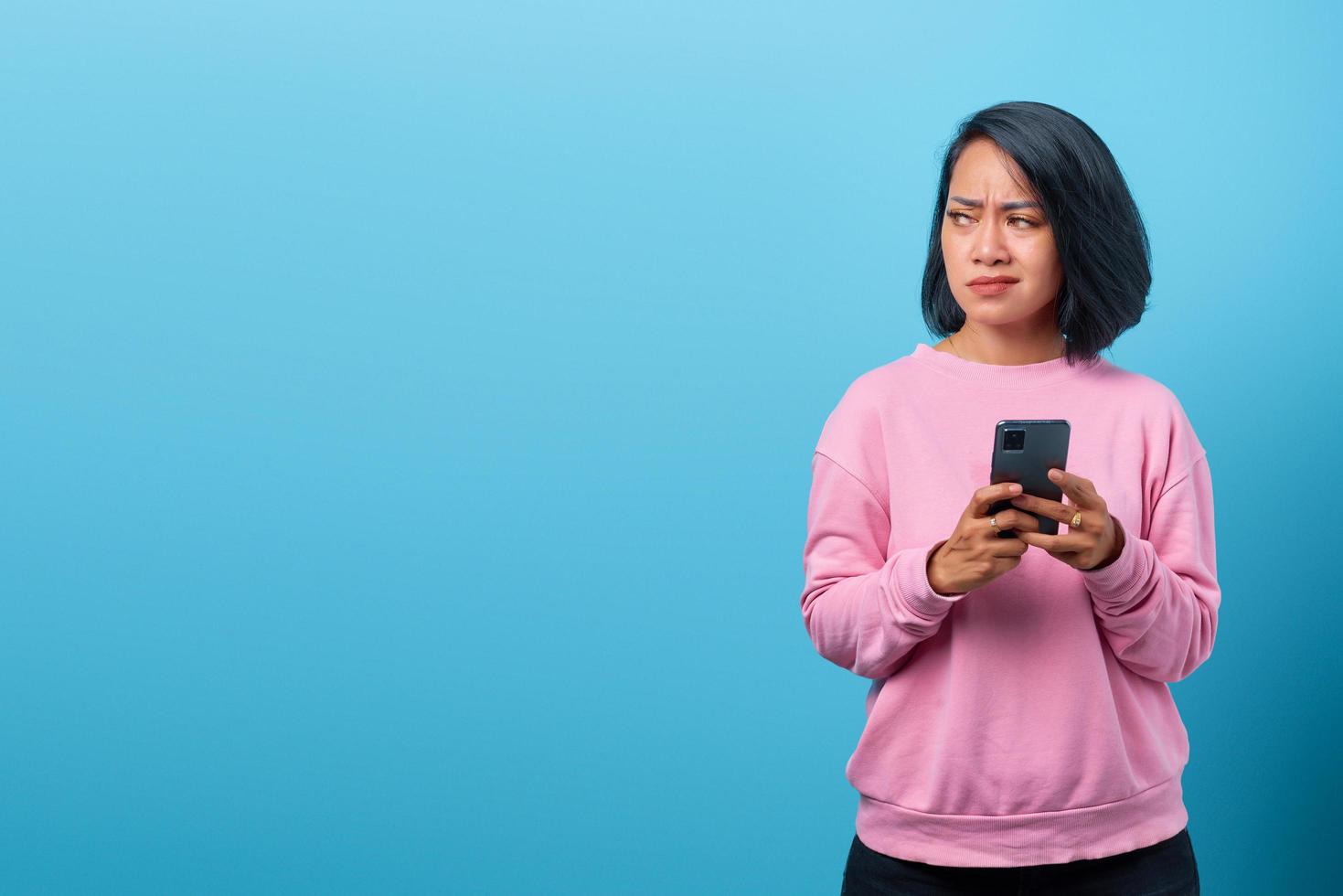 Joven mujer asiática sosteniendo smartphone infeliz mirando hacia los lados foto
