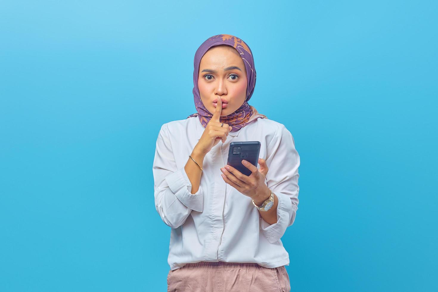 Beautiful Asian woman holding smartphone and making silent gesture photo