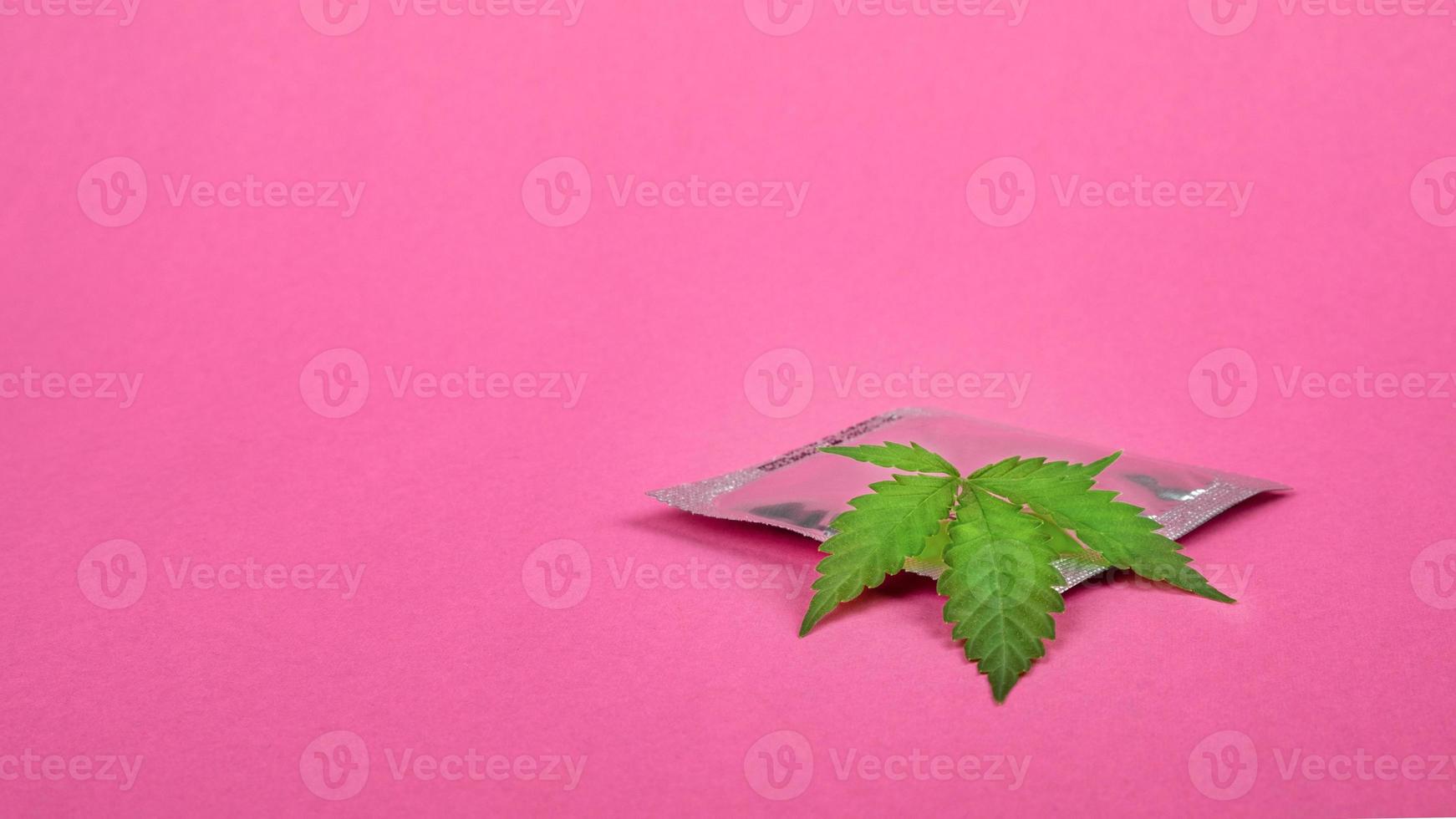 Condom and cannabis leaf on pink background copy space, contraception sex drugs concept. photo