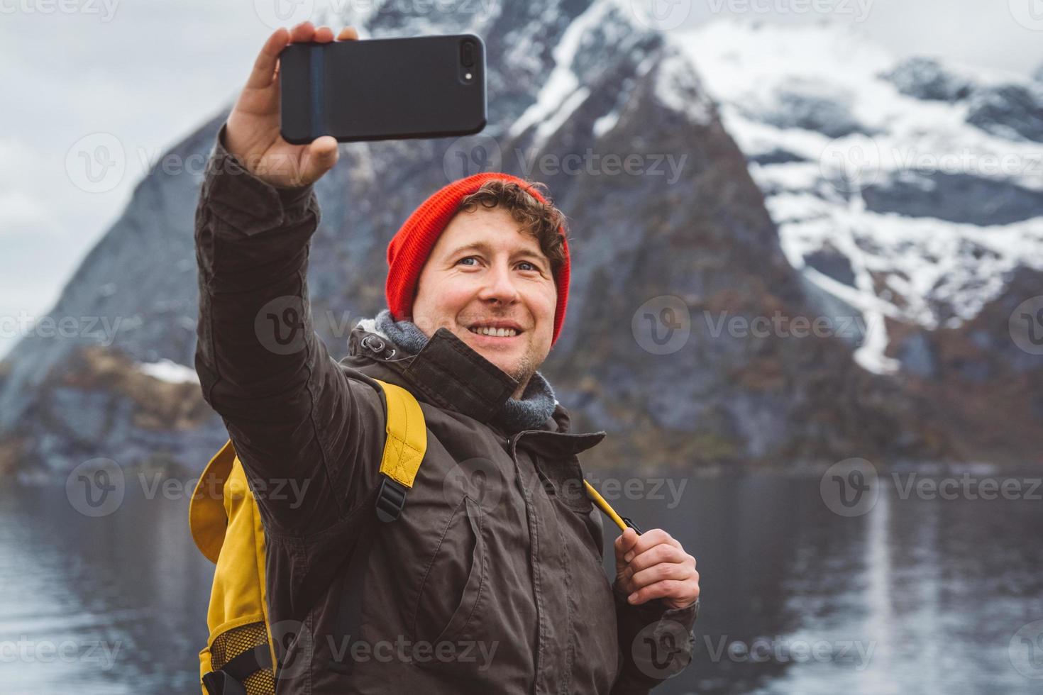 Hombre tomando selfie con montañas y lago detrás de él. foto