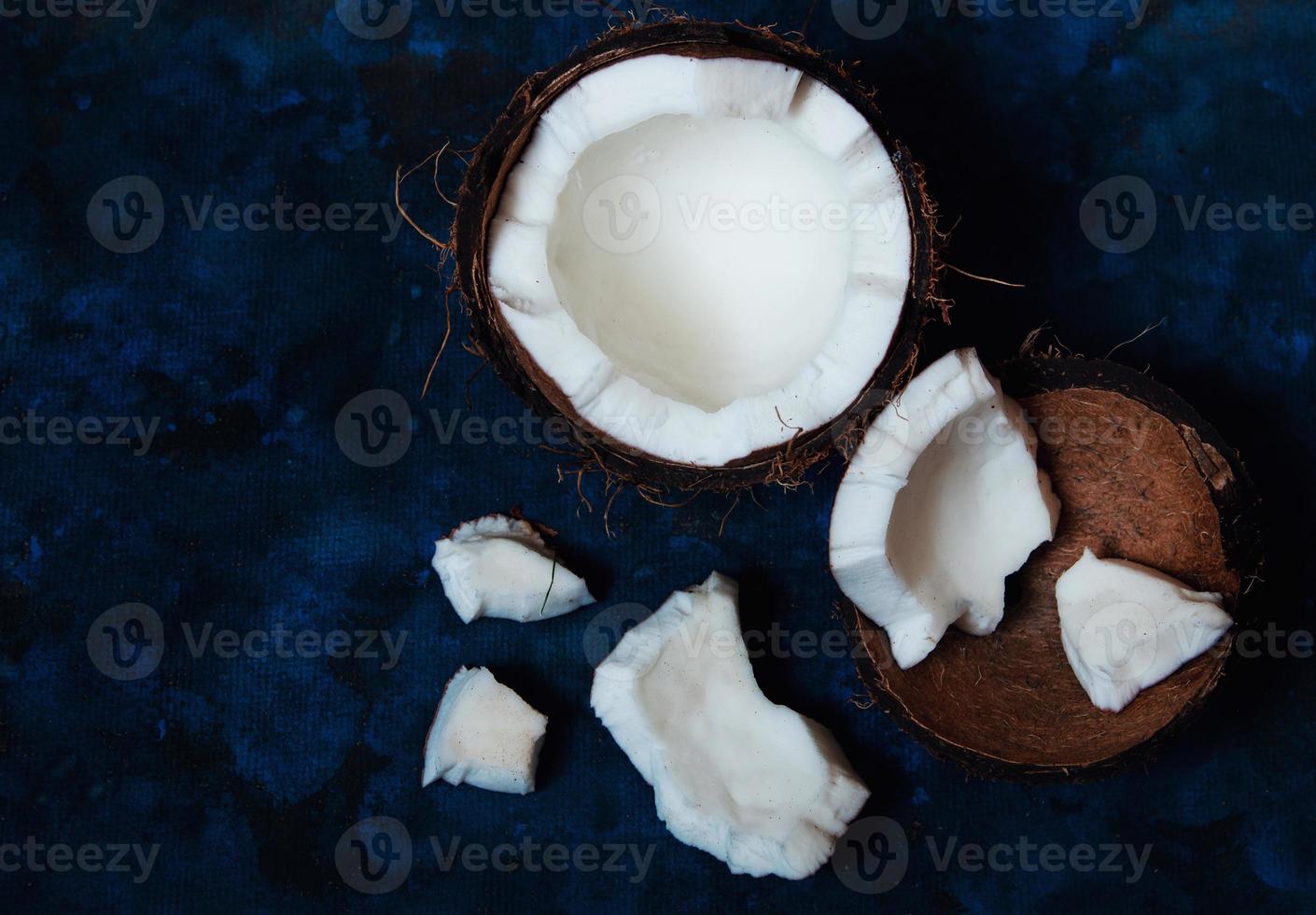 Open coconut lies on a dark blue background next to broken pieces photo