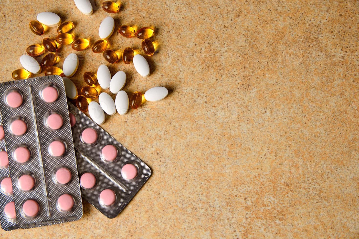 Blister with pink tablets and vitamin D and capsules with fish oil lie chaotically against the background of a sand countertop photo