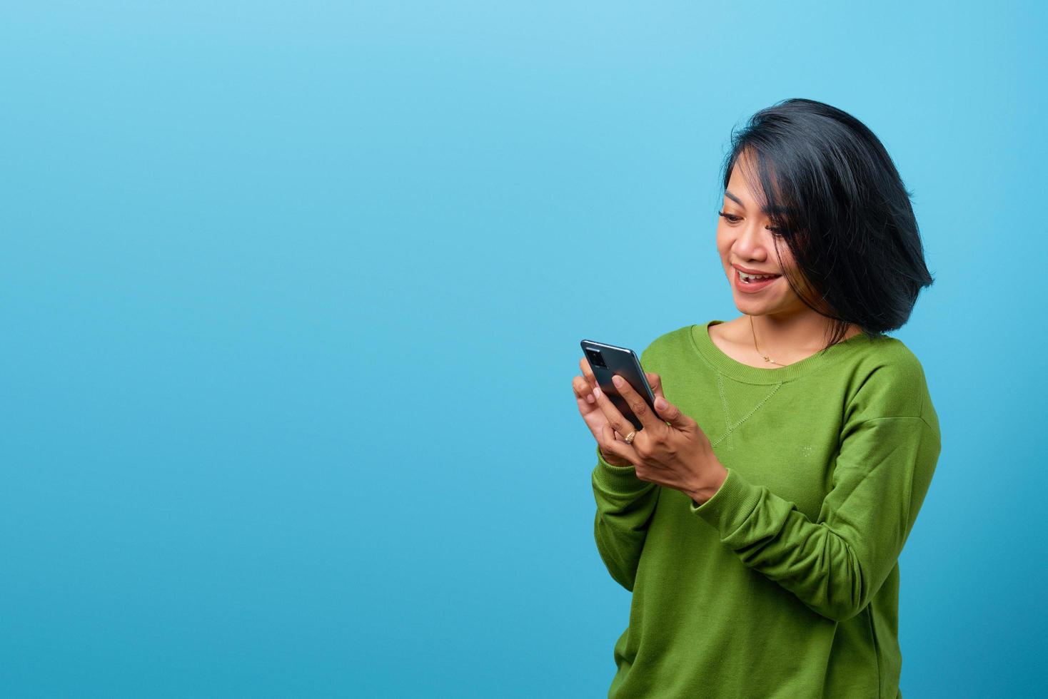 Beautiful Asian woman smiling using mobile phone on blue background photo