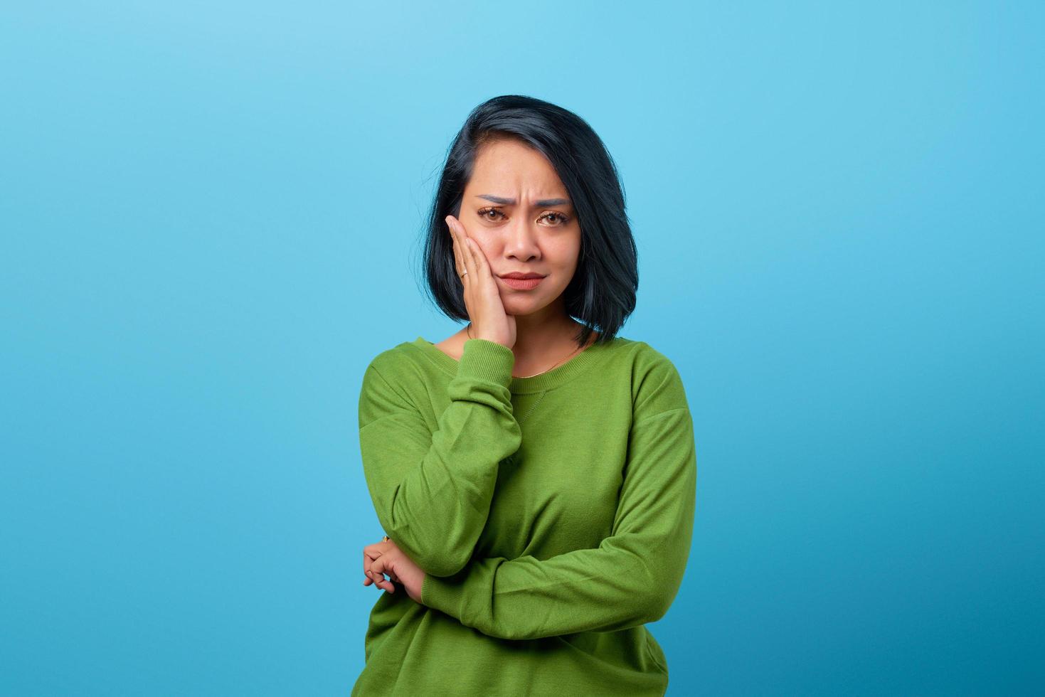 Asian woman touching cheek with bored expression on blue background photo