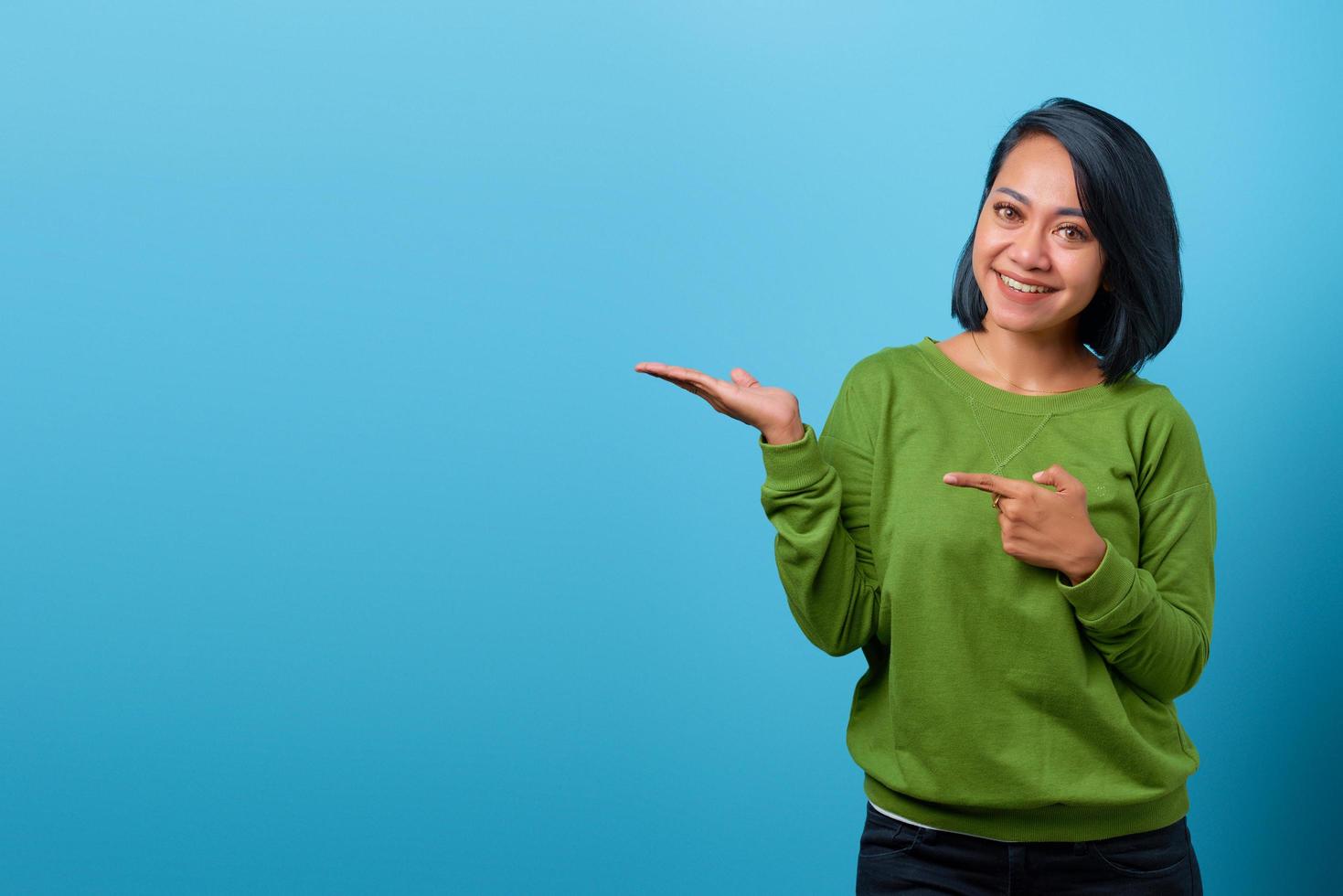 Retrato de mujer asiática sonriente mostrando el producto sobre fondo azul. foto