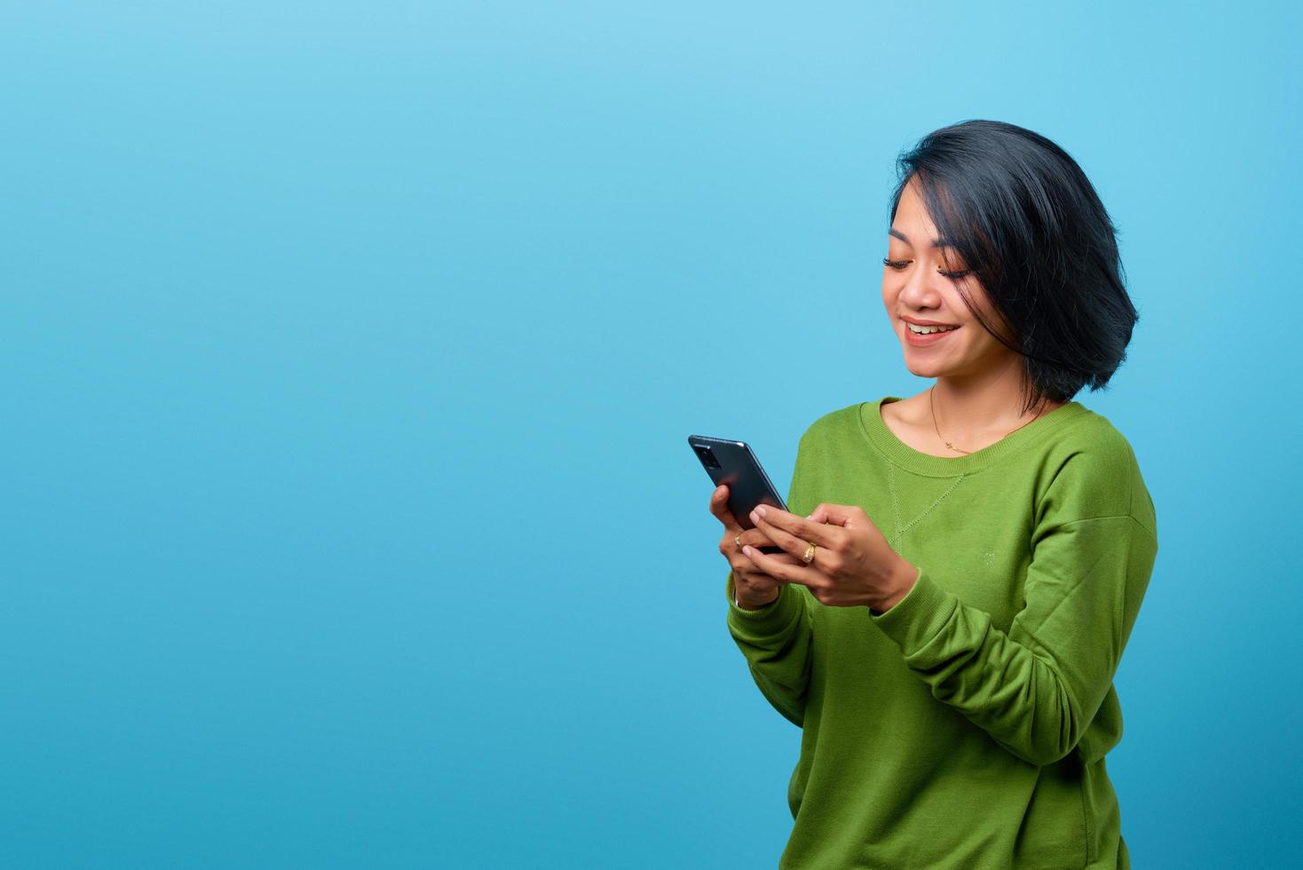 Hermosa mujer asiática sonriendo mediante teléfono móvil sobre fondo azul. foto