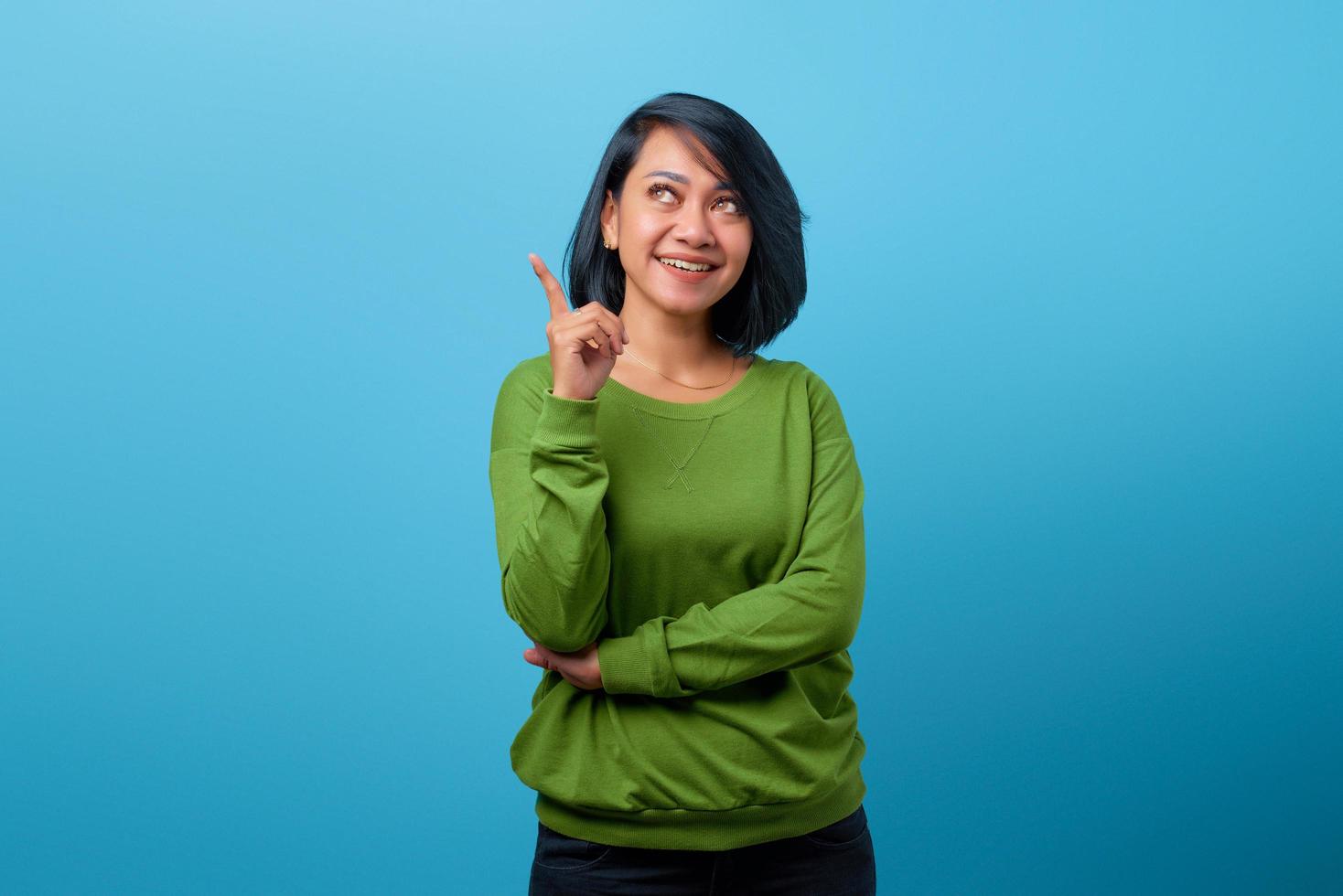 Atractiva mujer asiática con una sonrisa y apuntando hacia arriba con el dedo foto