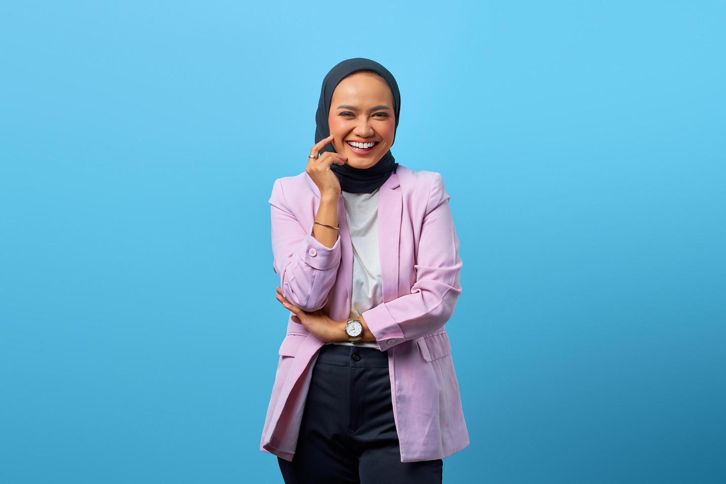 Cheerful Asian woman while touching cheek over blue background photo