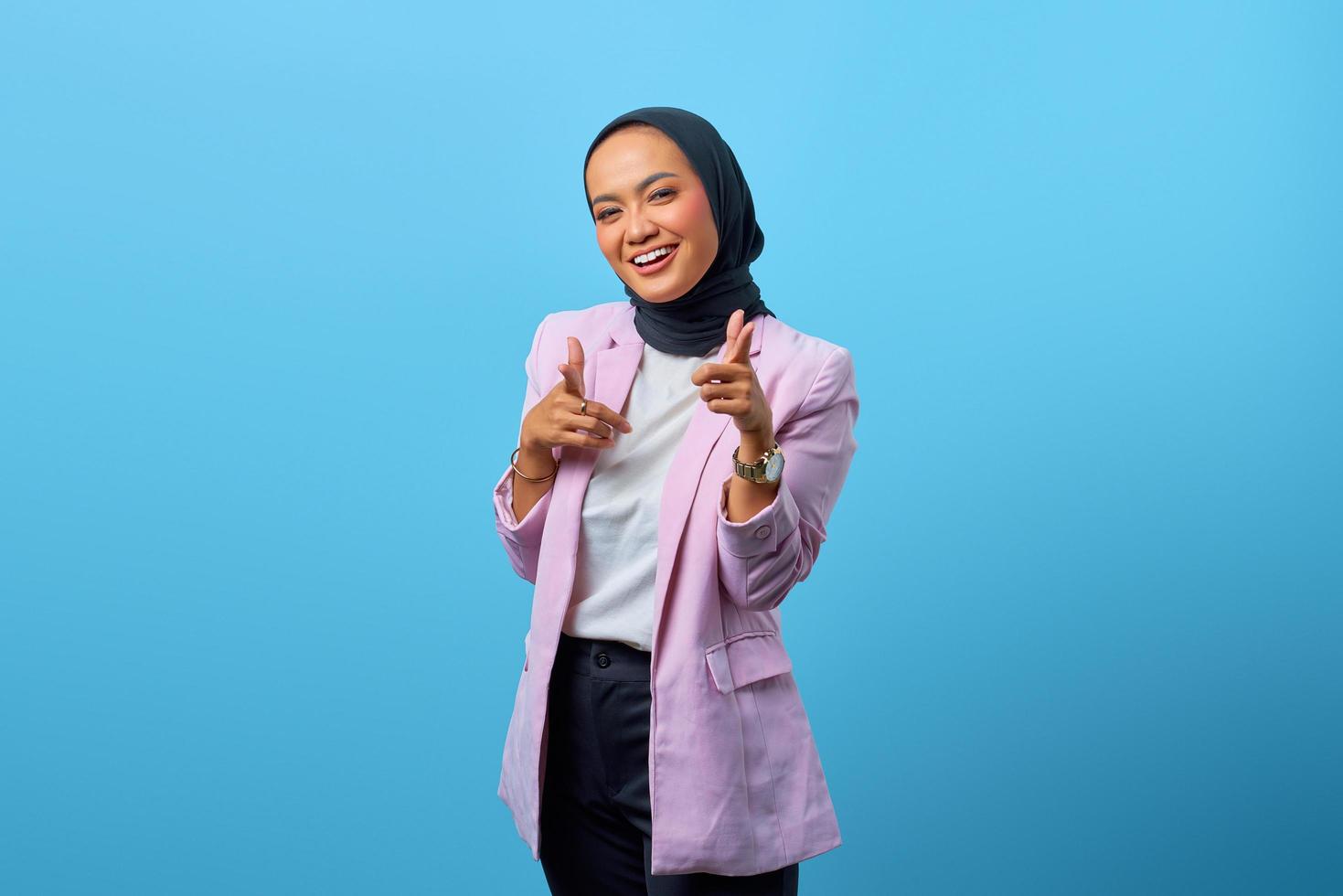 Alegre mujer asiática apuntando con el dedo a la cámara sobre fondo azul. foto