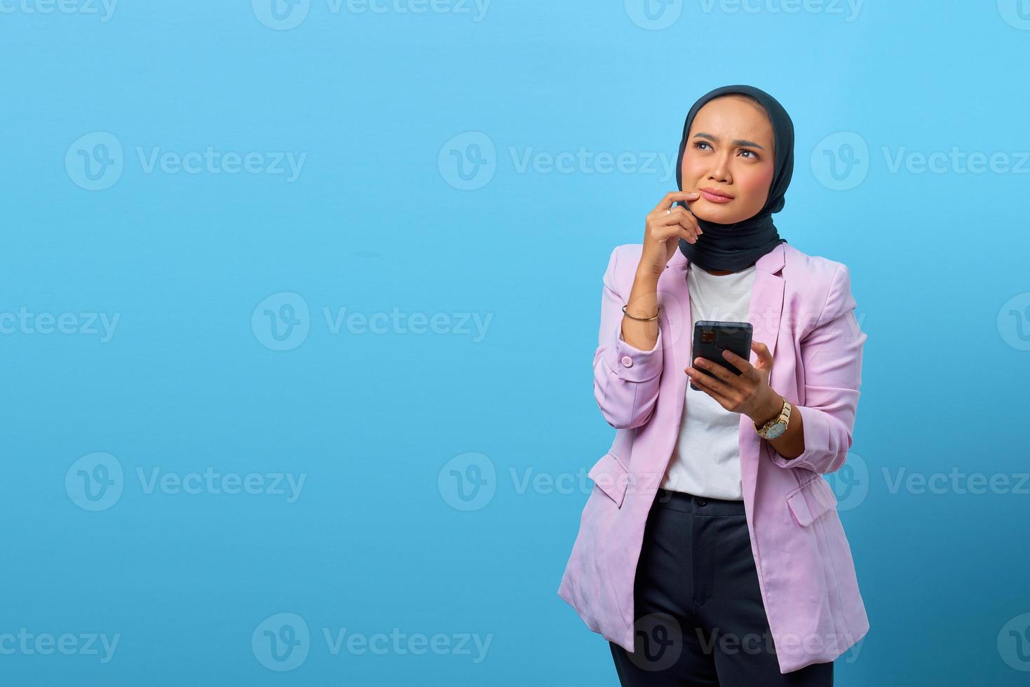 Hermosa mujer asiática piensa en algo y sostiene el teléfono móvil foto