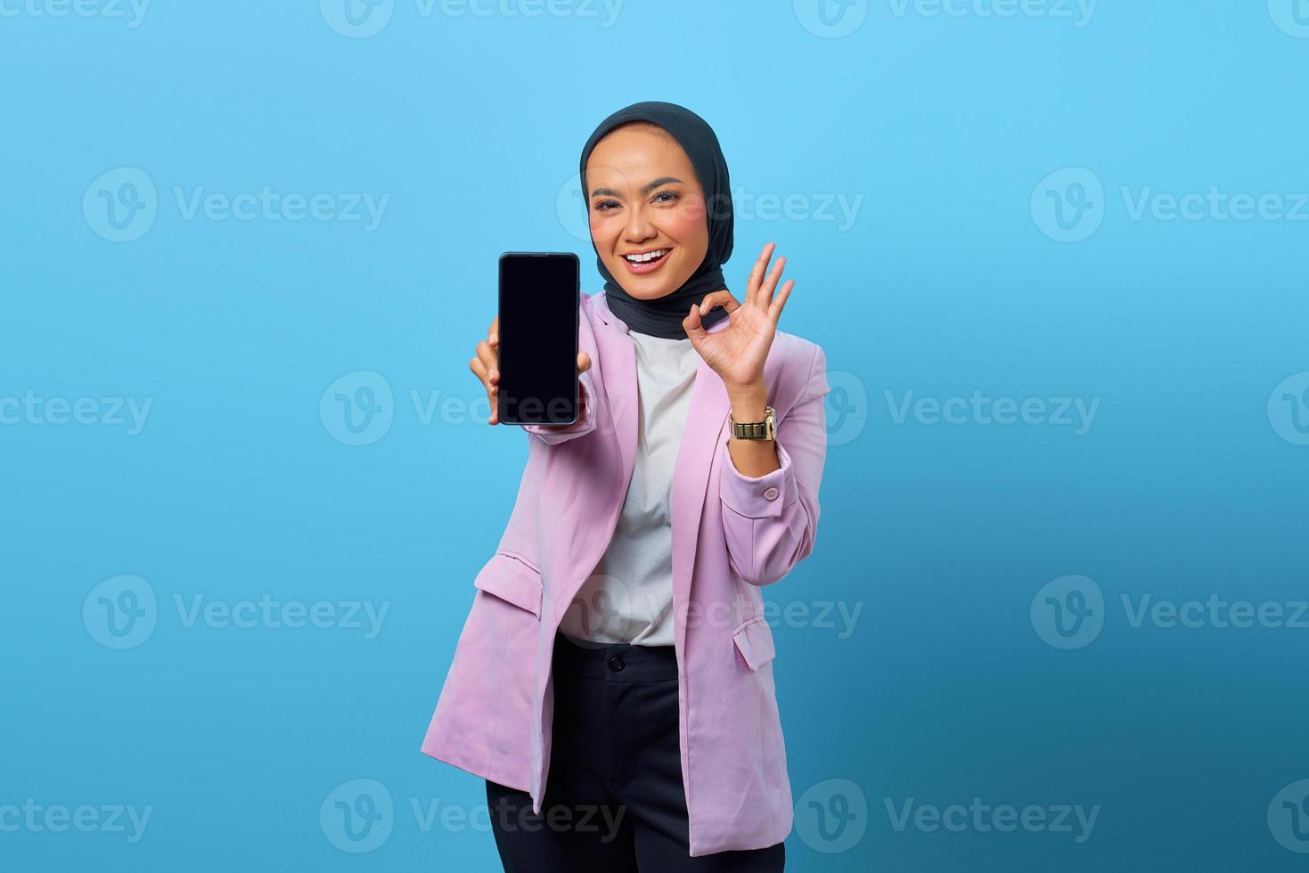 Mujer asiática que muestra la pantalla en blanco del teléfono inteligente y gesticula el signo bien foto