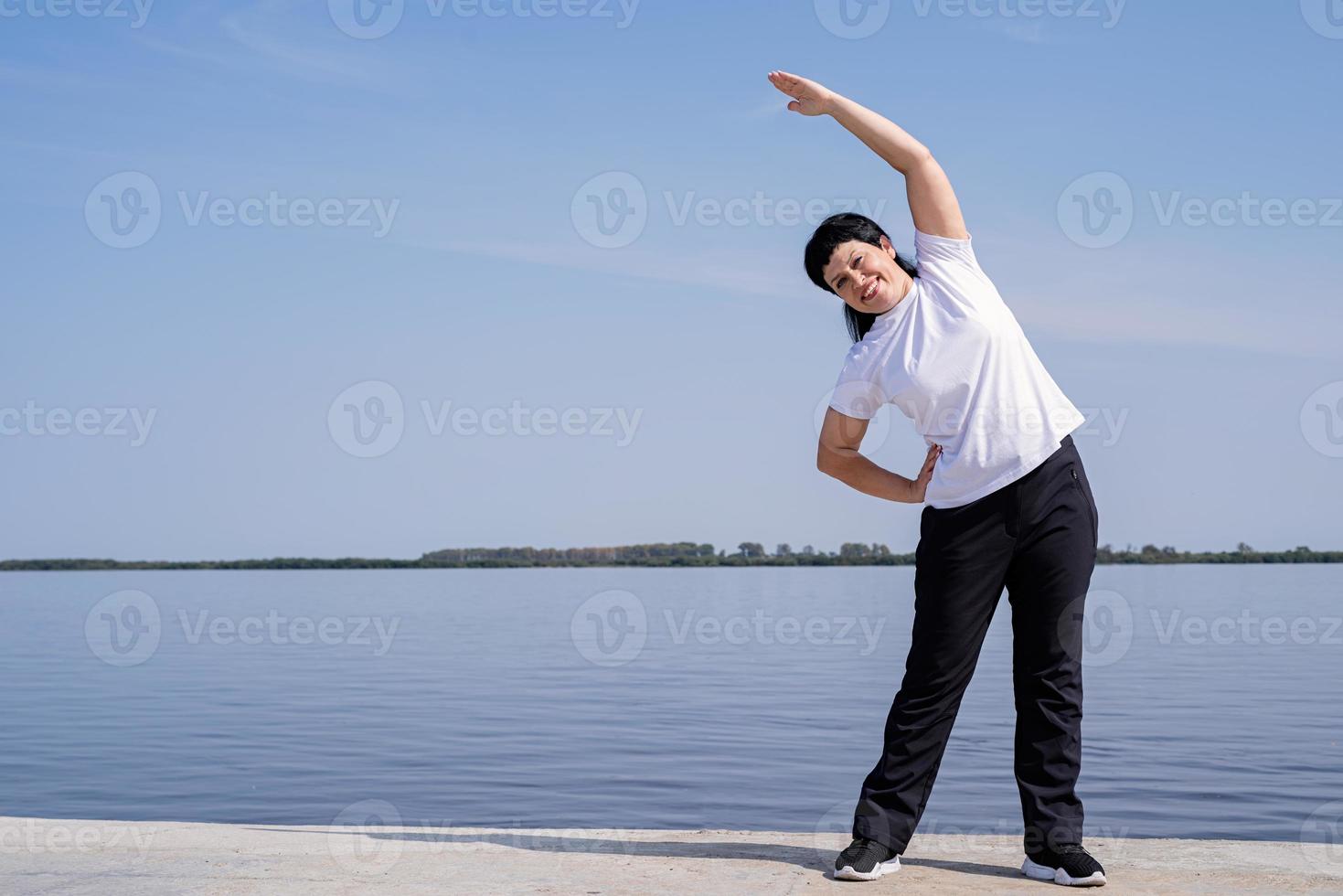 Active and happy senior woman doing stretching near the riverside photo