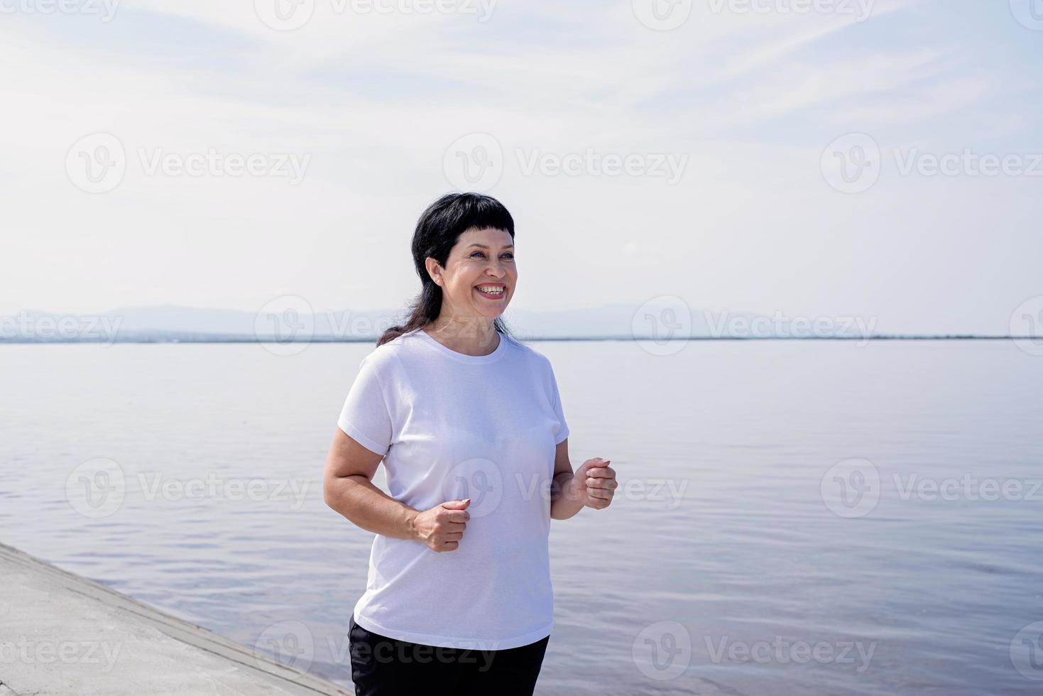 Active laughing senior woman jogging near the riverside photo