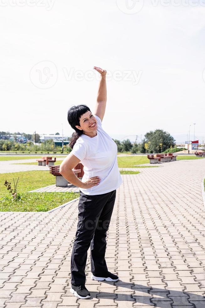 Smiling senior woman warming up stretching outdoors in the park photo