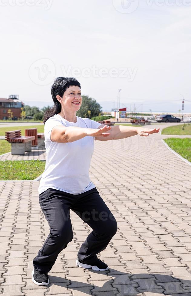 Sonriente mujer mayor en cuclillas al aire libre en el parque foto