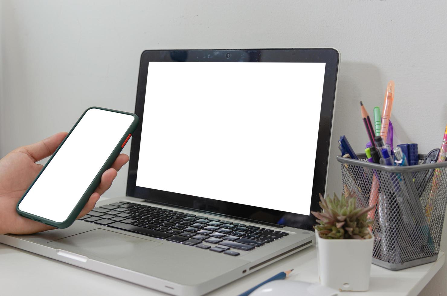 simulacro de mano que sostiene la computadora portátil de pantalla en blanco blanco del teléfono inteligente en el escritorio foto